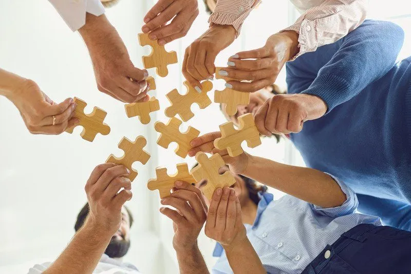 Several hands joining wooden puzzle pieces together